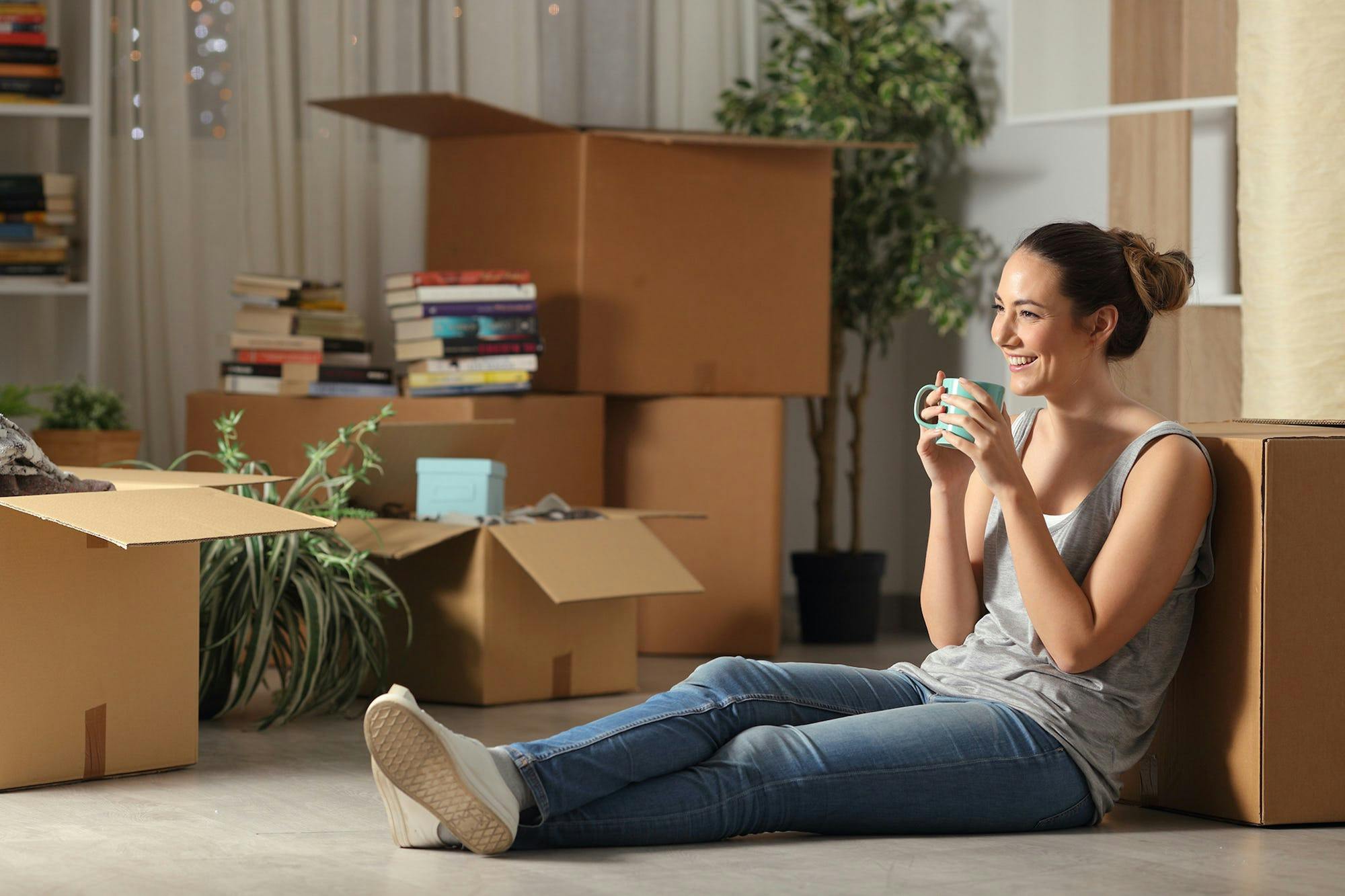 A woman enjoys a cup of tea against a moving box as she takes a break from unpacking belongings in a new rental home