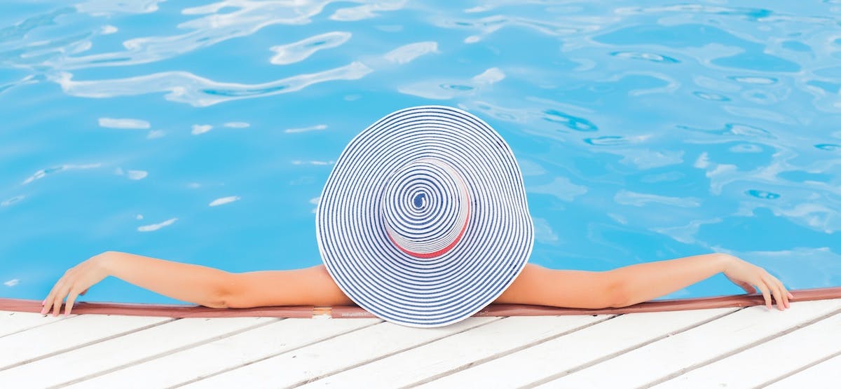 An image of a woman relaxing in a swimming pool wearing a large blue and white striped hat, enjoying her new home at the peak demand time for rentals.