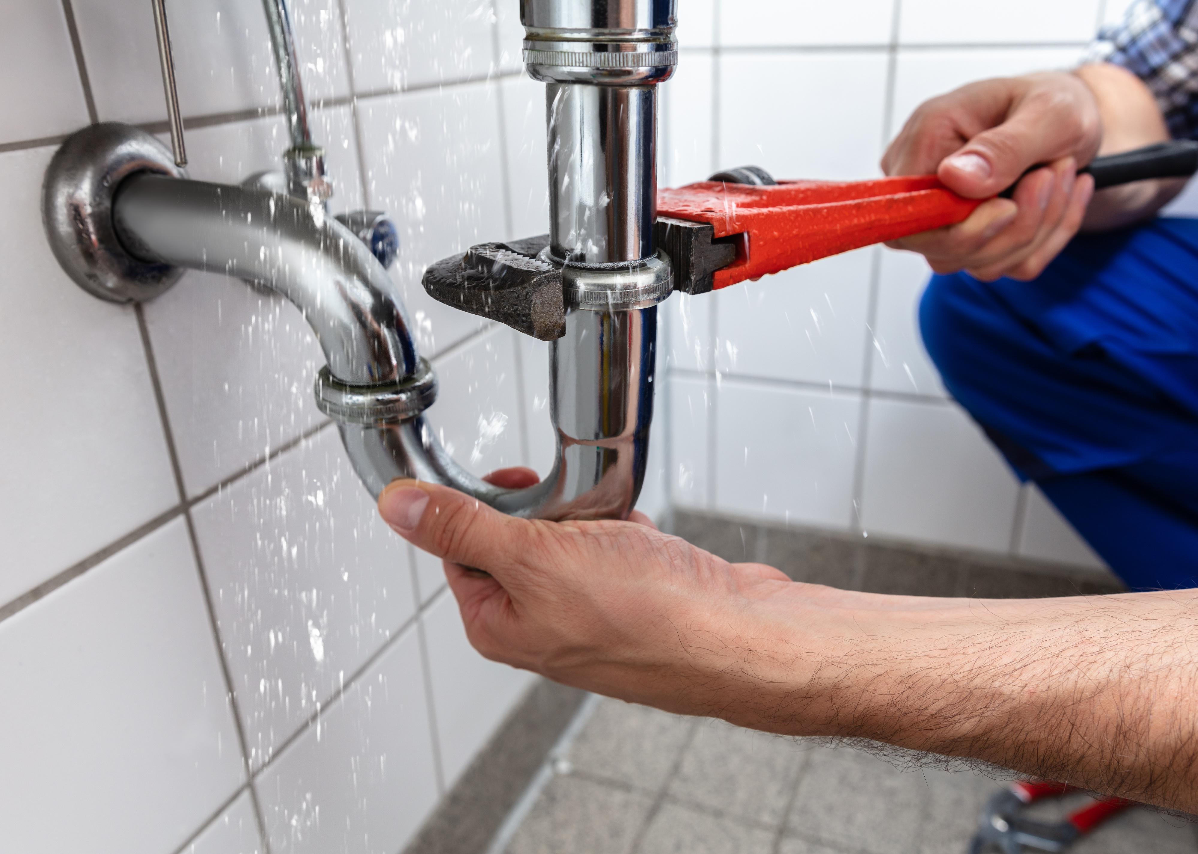 A plumber uses a wrench to fix leaky pipes in a bathroom 