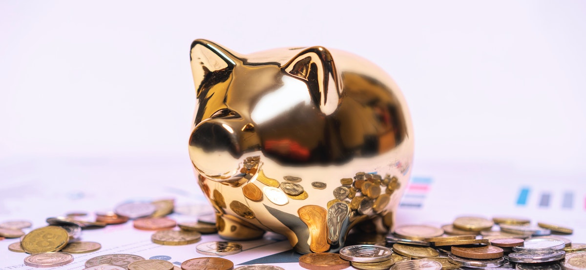 A gold shiny piggy bank sits among coins and spreadsheet charts, depicting how to do an accurate rental property cash flow analysis