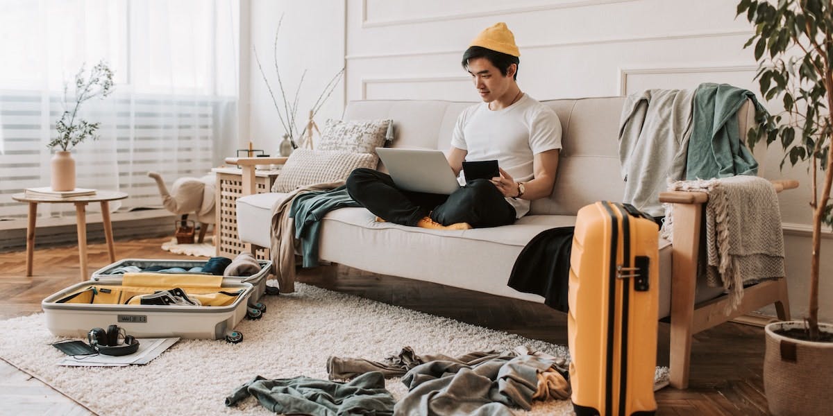 Photograph of a young male traveller getting comfortable in a messy lounge room with unpacked suitcases in a short-term rental property