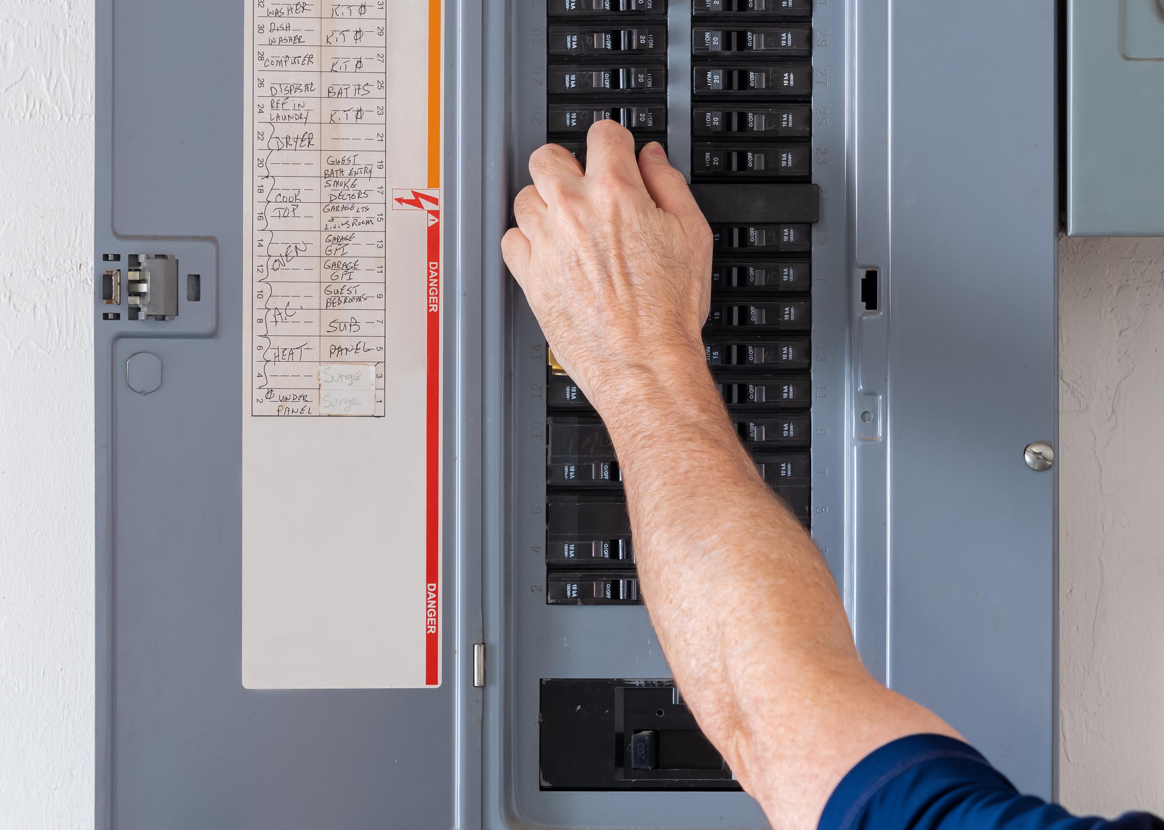 A hand reaching into an open electrical panel