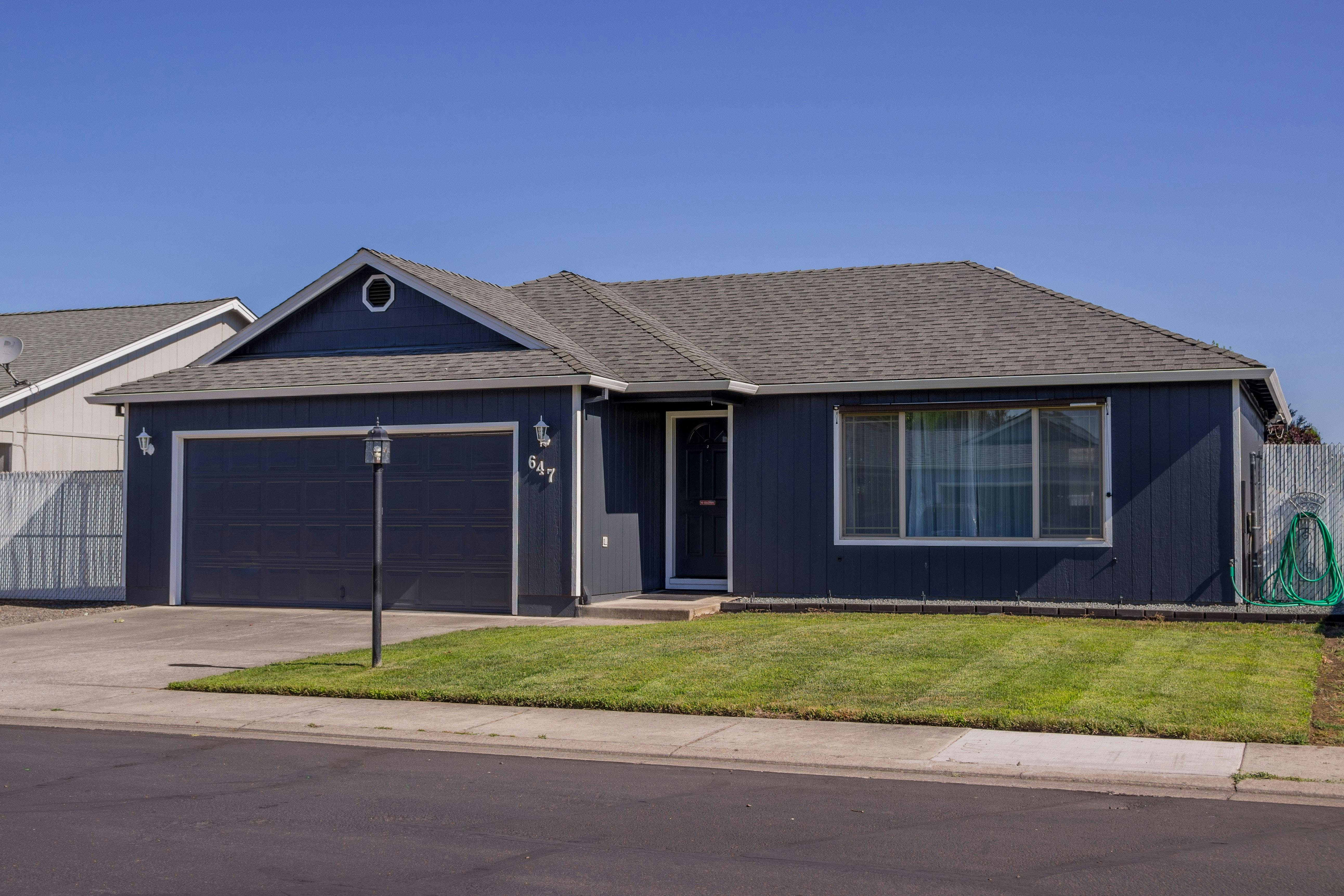 An image of a dark grey single-family home with neat lawn against a blue sky, an ideal first-time rental home. 