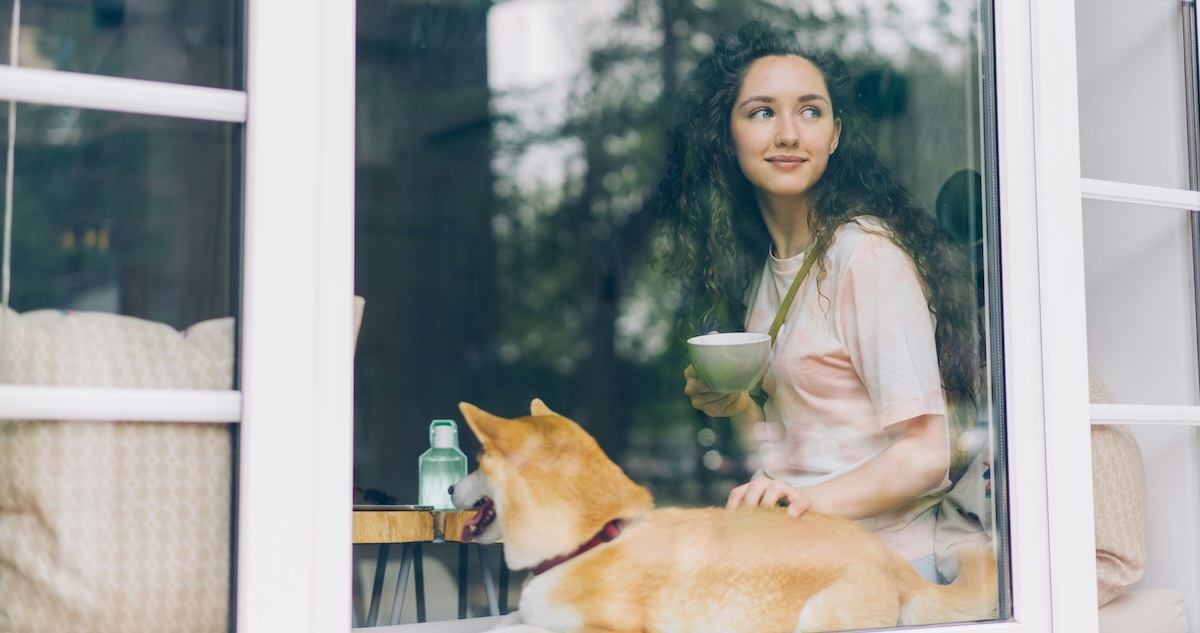 A Gen Z woman enjoys a cup of tea in the windowsill with her pet dog