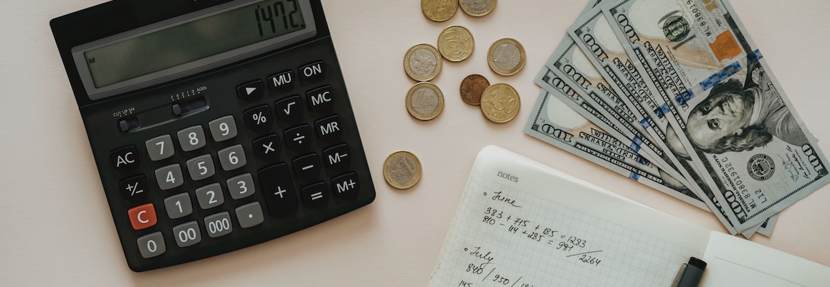 A black calculator with a note pad and cash, working out monthly expenses and passive income needs 