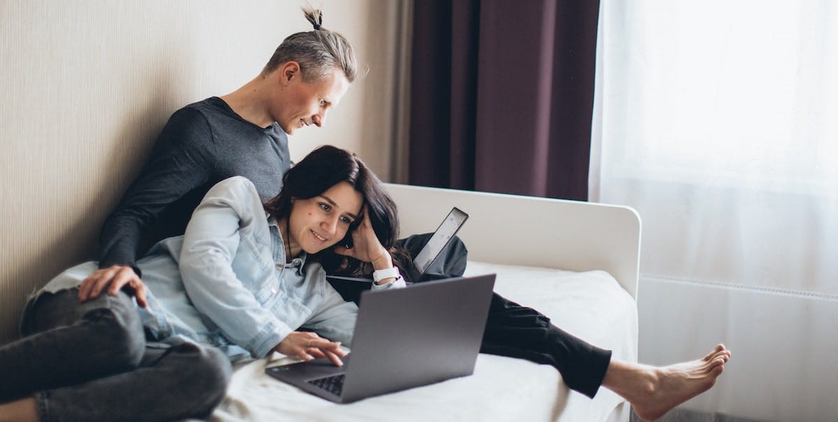 A couple work together on the couch, using a laptop and tablet to access technology to manage their rental home and property management services