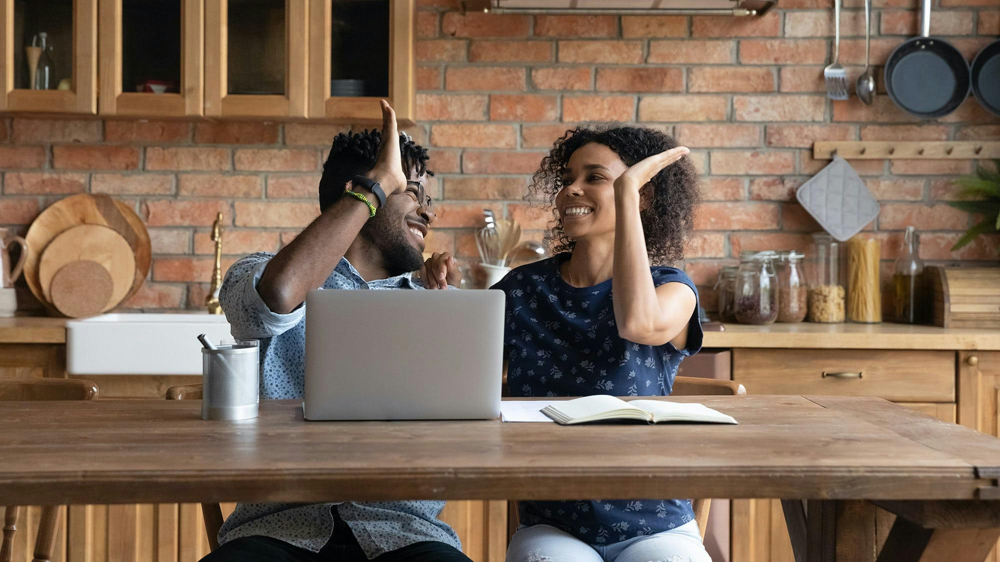 Young couple high-fiving in the kitchen while looking at a laptop, securing guaranteed rent for their property