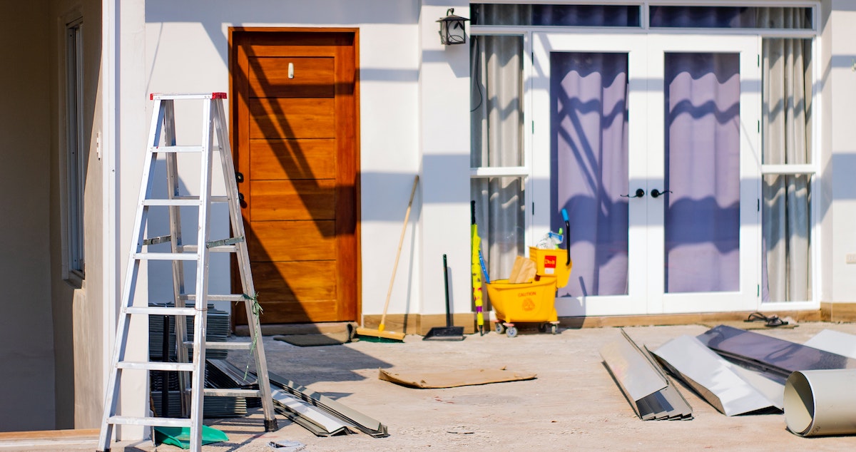 A photo of a property during a home remodel, with a ladder and construction materials outside the front door. Find out how to choose a home remodeling contractor