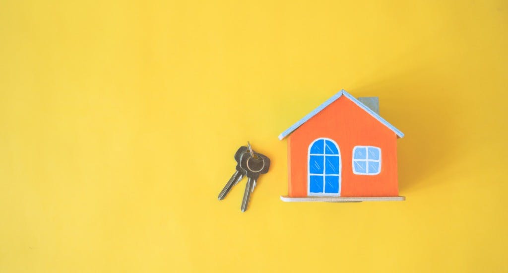 Yellow background with a set of house keys and a model of a small orange house, concept of home and property management
