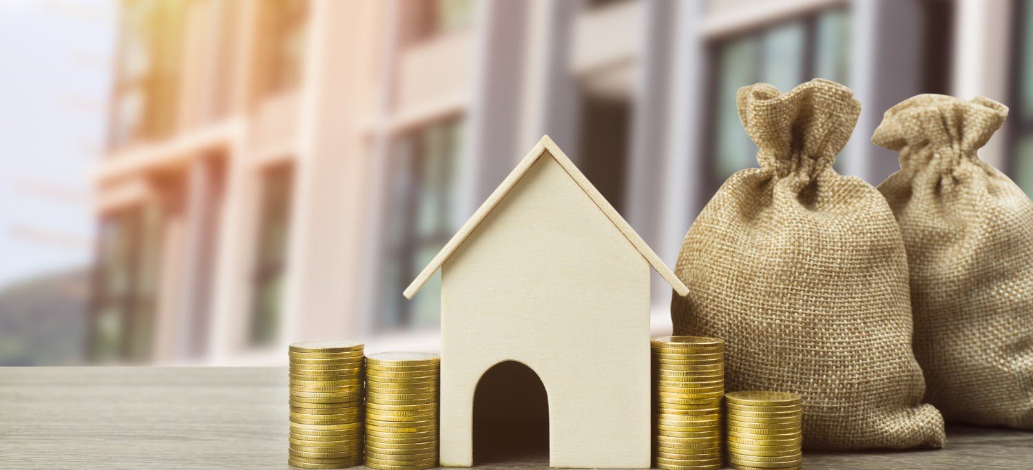 A model of a house besides coins and bags of money, depicting passive income earned by property on the rental market