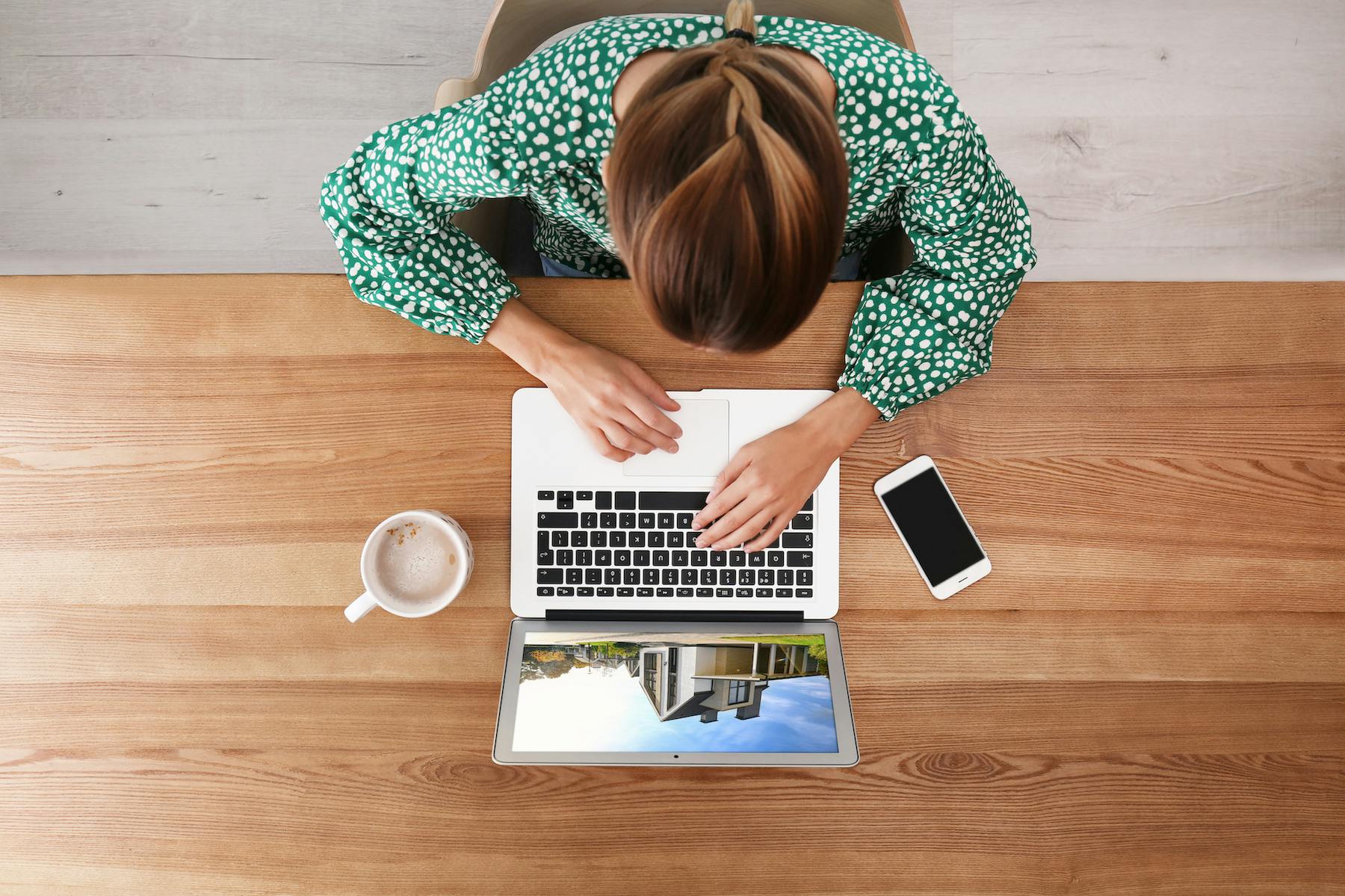 Birds-eye-view of a woman reviewing homes and property management information on her laptop with a phone and cup of tea