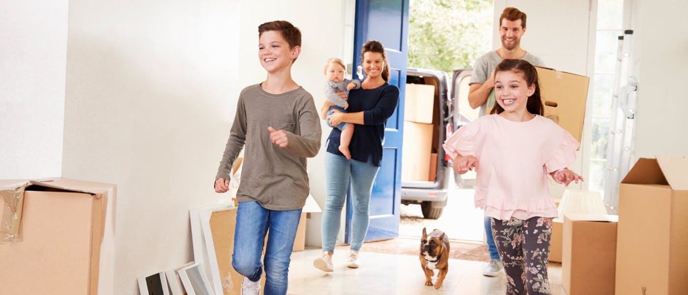 A family of five and a small dog run happily into a new home among moving boxes. Families can not be discriminated against under Fair Housing Laws.