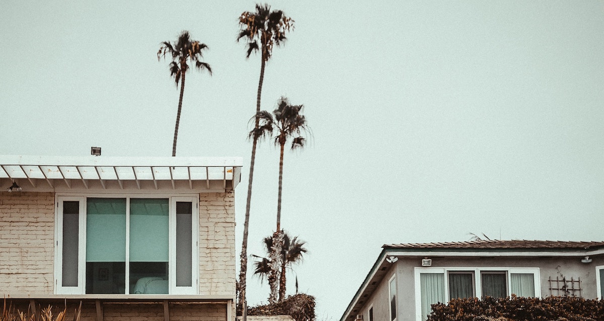 An image of two beachfront homes in San Diego with palm trees in the background. Learn more about investing in real estate and rental properties in San Diego. 