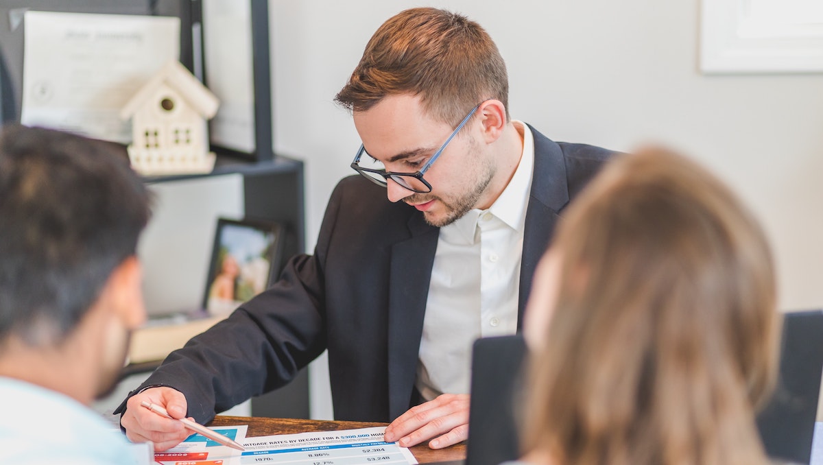A property manager in a suit and glasses discusses property management fees with homeowners. Find out how to calculate the ROI of a property manager. 