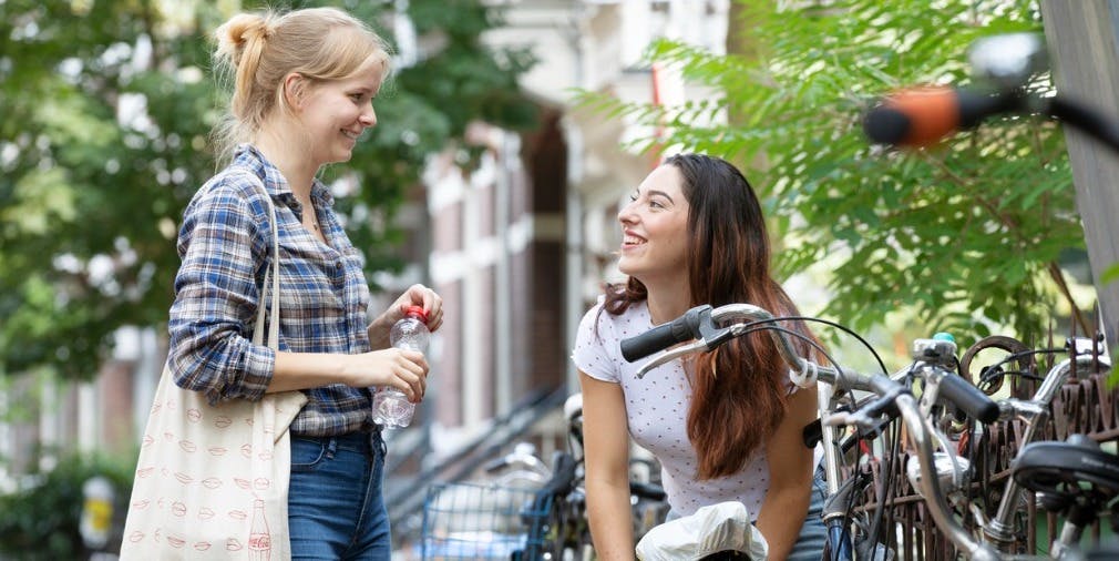 Two young women talk in their neighborhood next to a row of bikes and homes