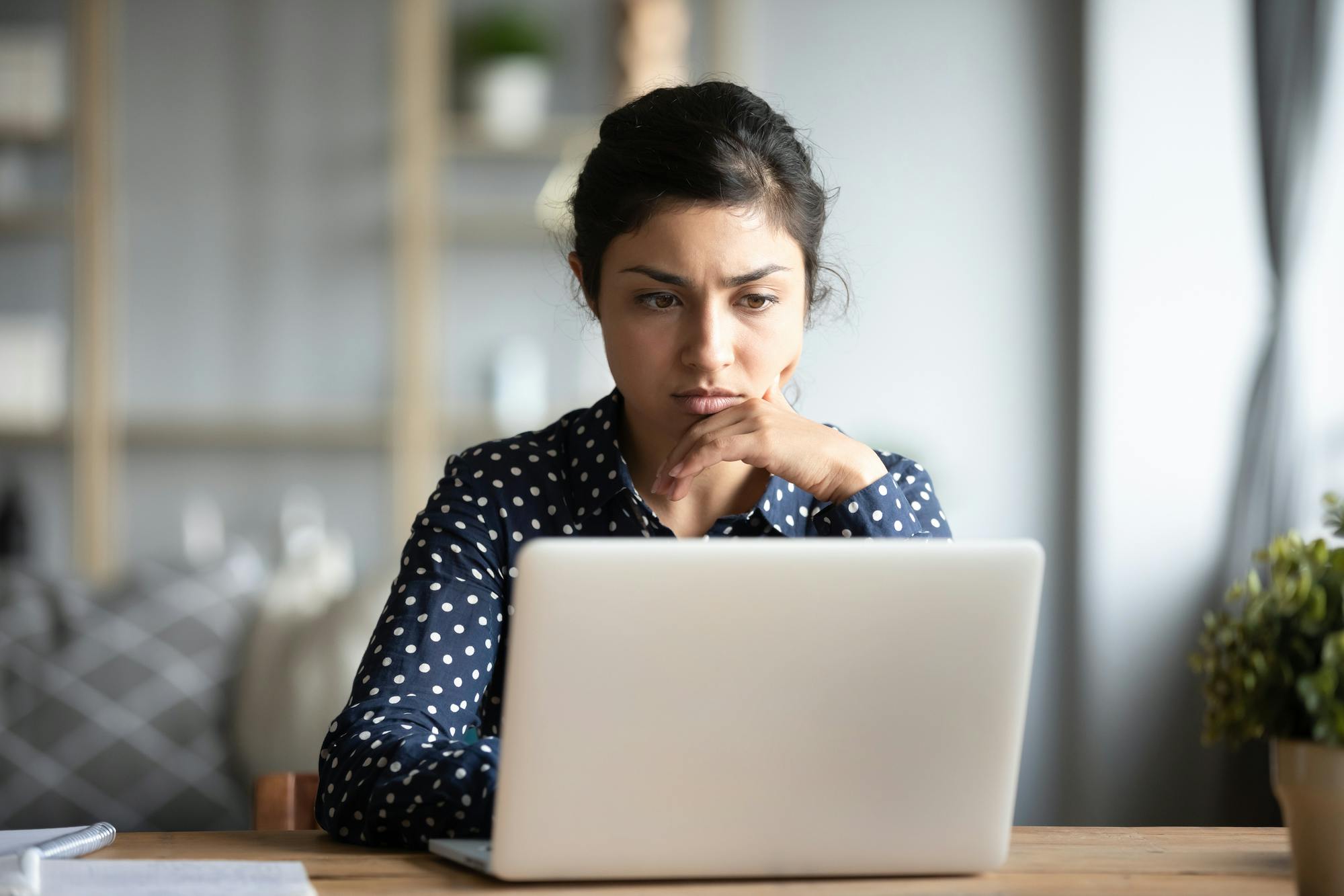 A young woman looks at her laptop with concern and/or confusion