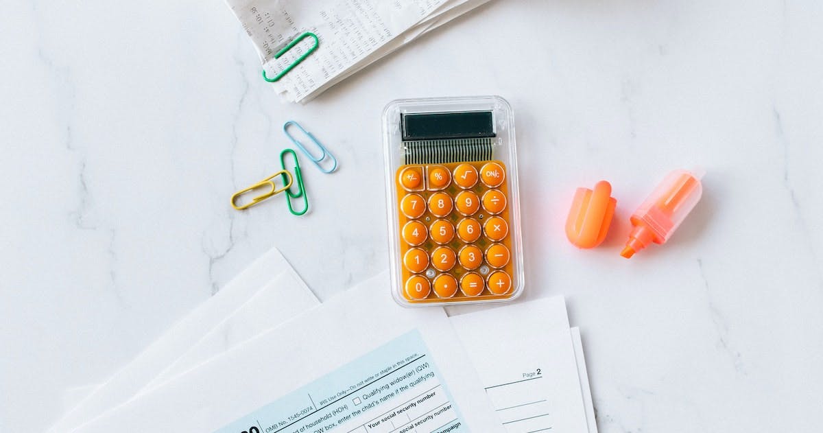 A calculator with orange buttons sits alongside a highlighter, receipt and individual tax return paperwork, depicting tax deductions for property management fees