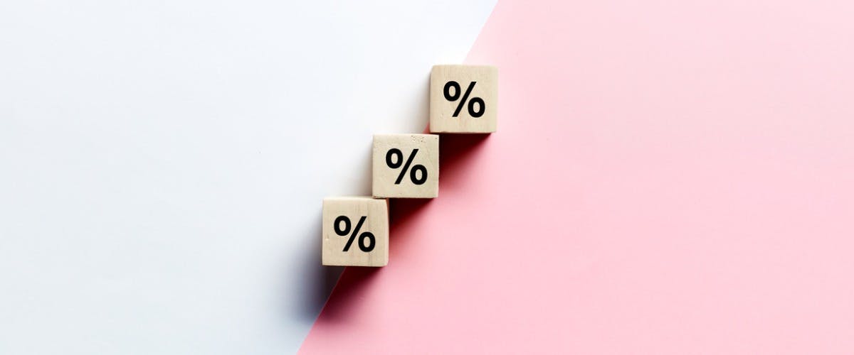 A white and pink background with three wooden tiles displaying the percentage sign, showing a rise in interest rates for homeowners