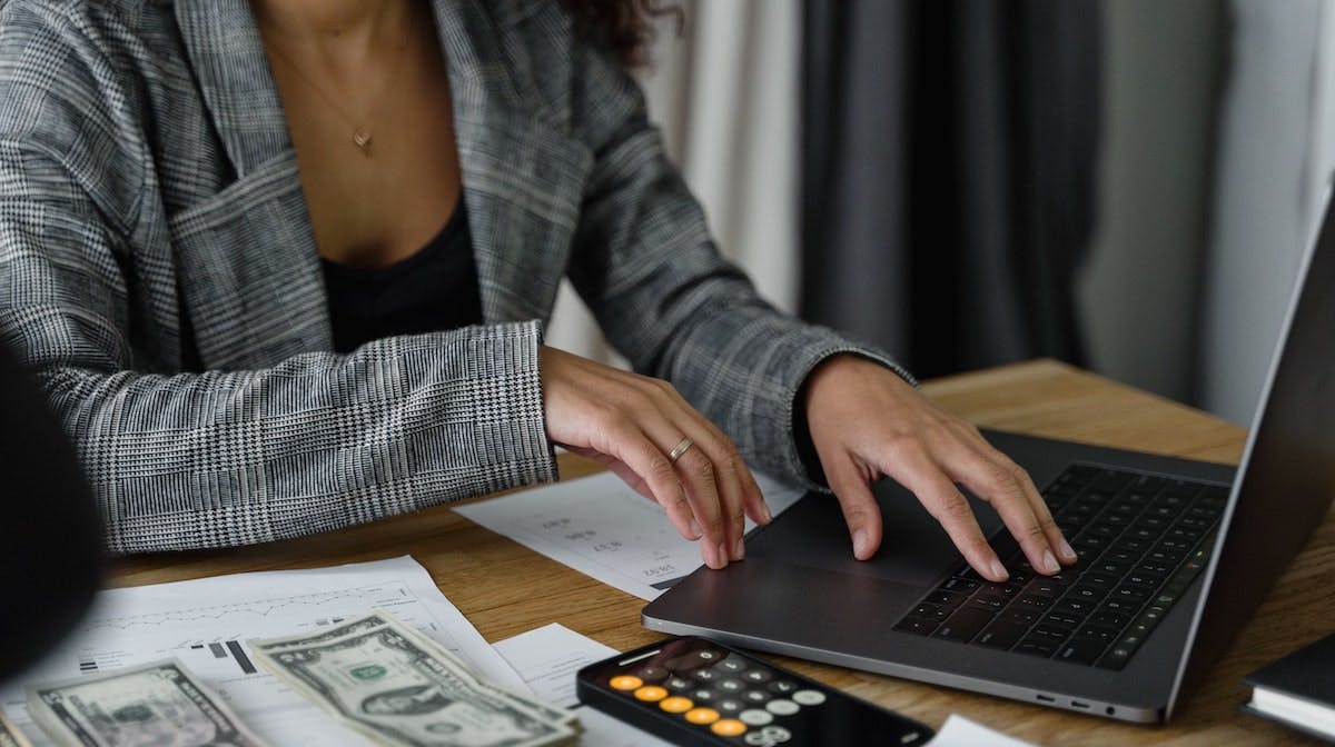 A woman manages her rental home finances on her laptop, with a calculator and cash at her side. 
