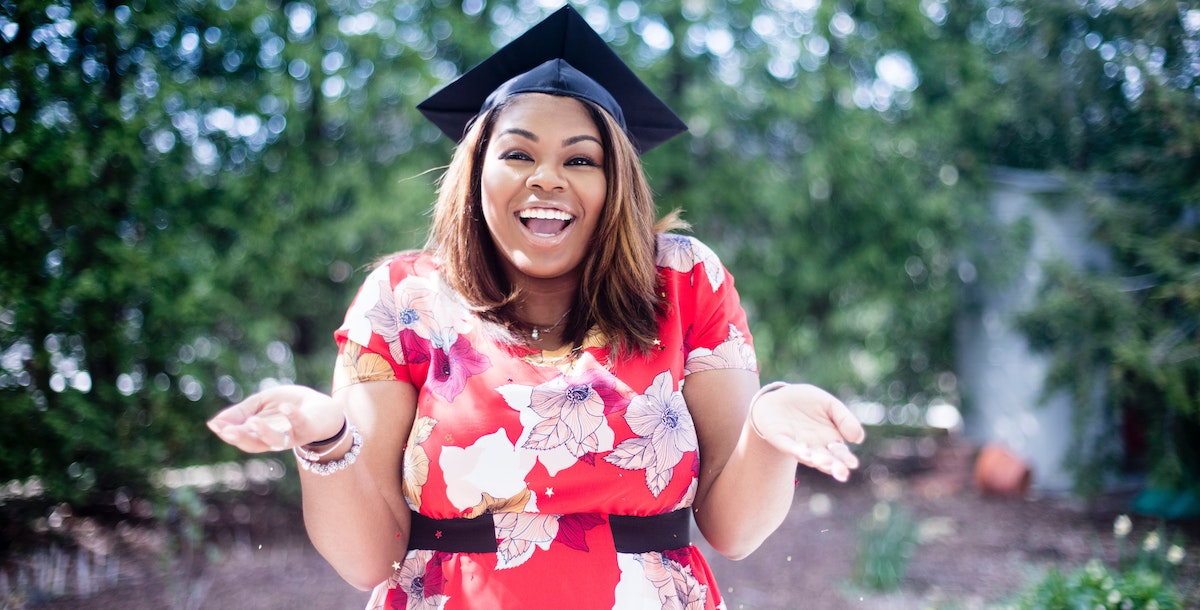 A woman of color is wearing a red floral dress and a graduation cap, smiling and shrugging happily. In this article we ask "how will student debt forgiveness affect the real estate market?"