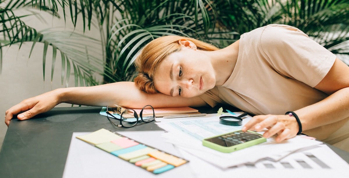 A young woman feels tired calculating tax deductions on her real estate investment/rental property, laying her head down on the desk while using a calculator