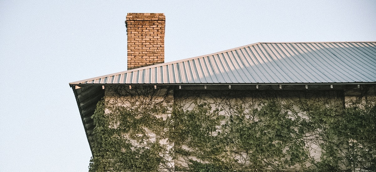 A chimney on a white roof for a home in Texas, with vines growing beneath