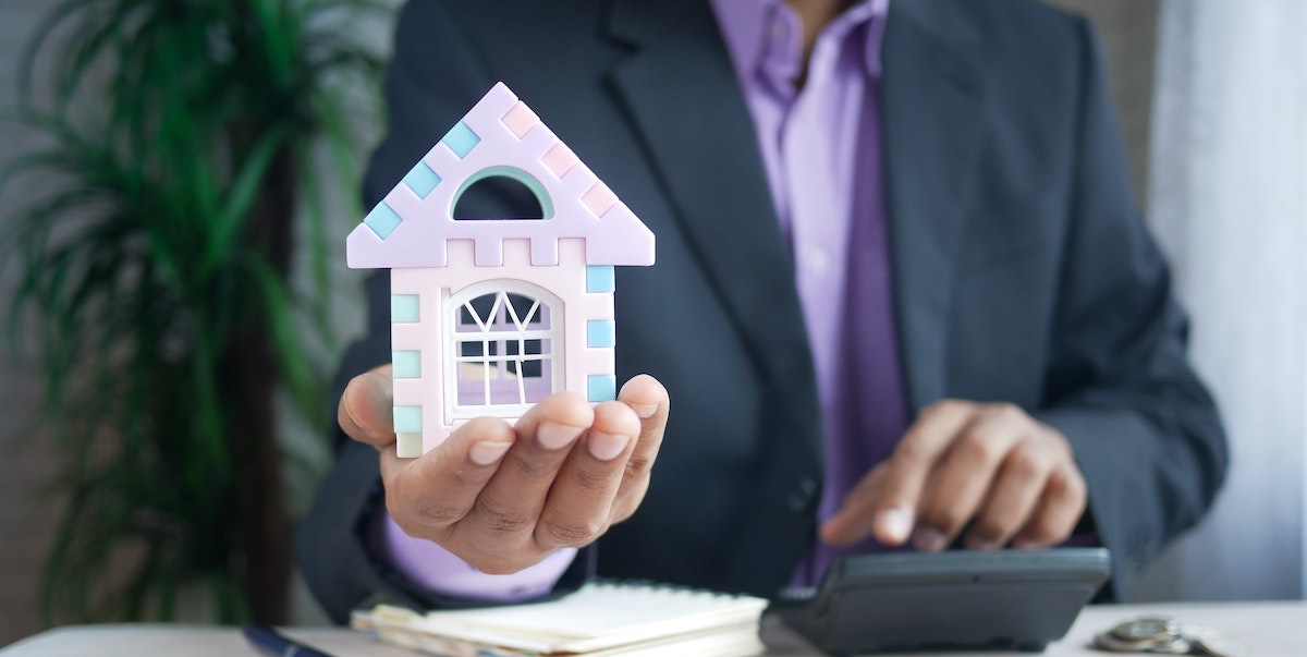 A property manager in a business suit and purple shirt holds a model of a home in one hand and calculates fees with the other. Learn more about property management fees and how much property managers charge.