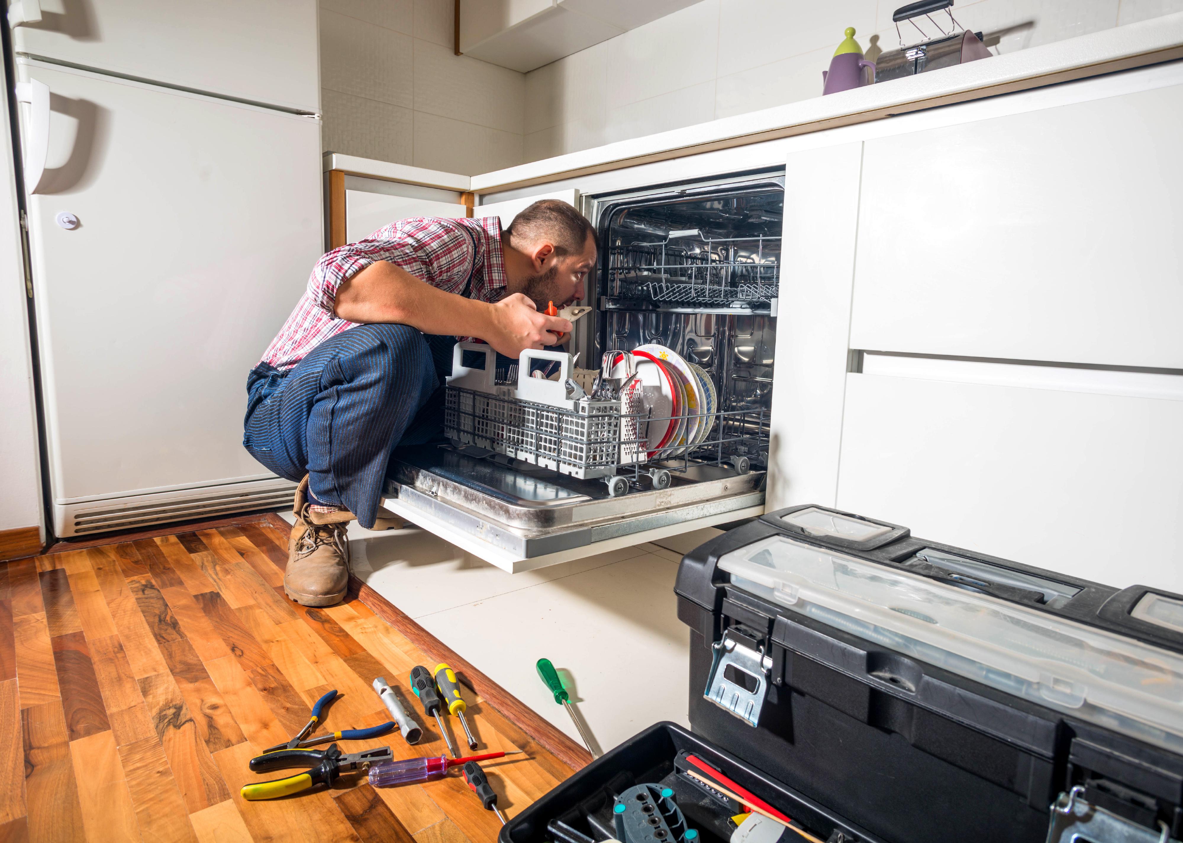 A man repairs a dishwasher in a kitchen 
