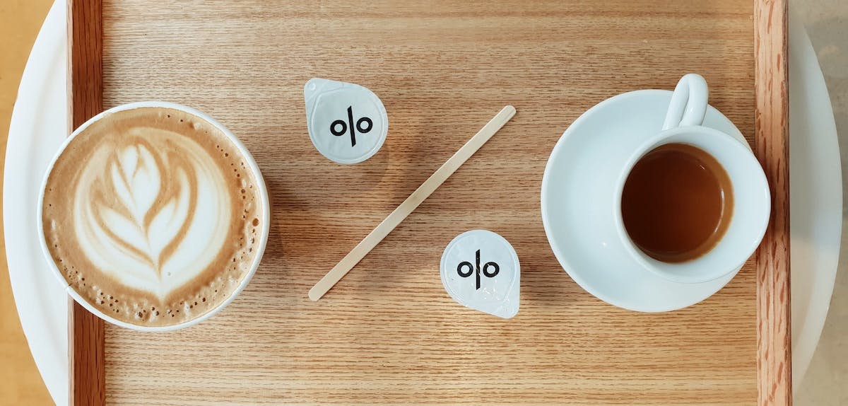 Debt-to-income ratio is depicted with two cups of coffee, one with milk and one without. The percentage signs are on crema cups and a wooden stirrer. 