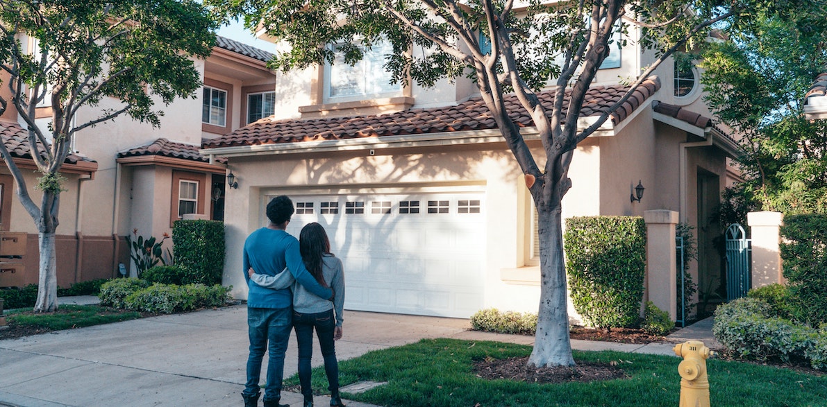 A couple admires a well-presented home with neat laws. HOAs can be great for the community, but learn the HOA red flags to avoid. 