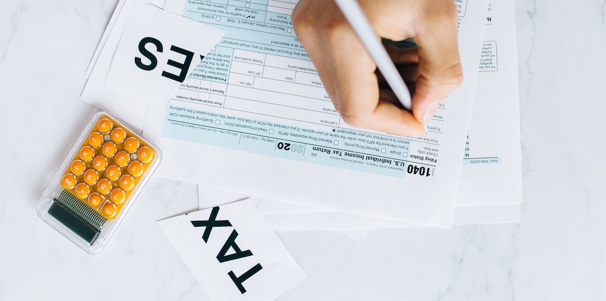 An image of a person filling out a 1040 Tax Return with a calculator, working out income and deductions such as if property management fees are tax deductible from rental income.  