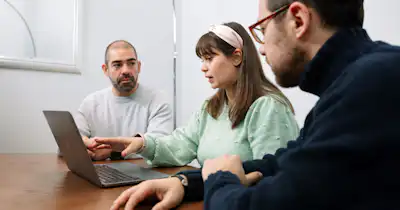 Three people in an office setting talking in front of a computer.