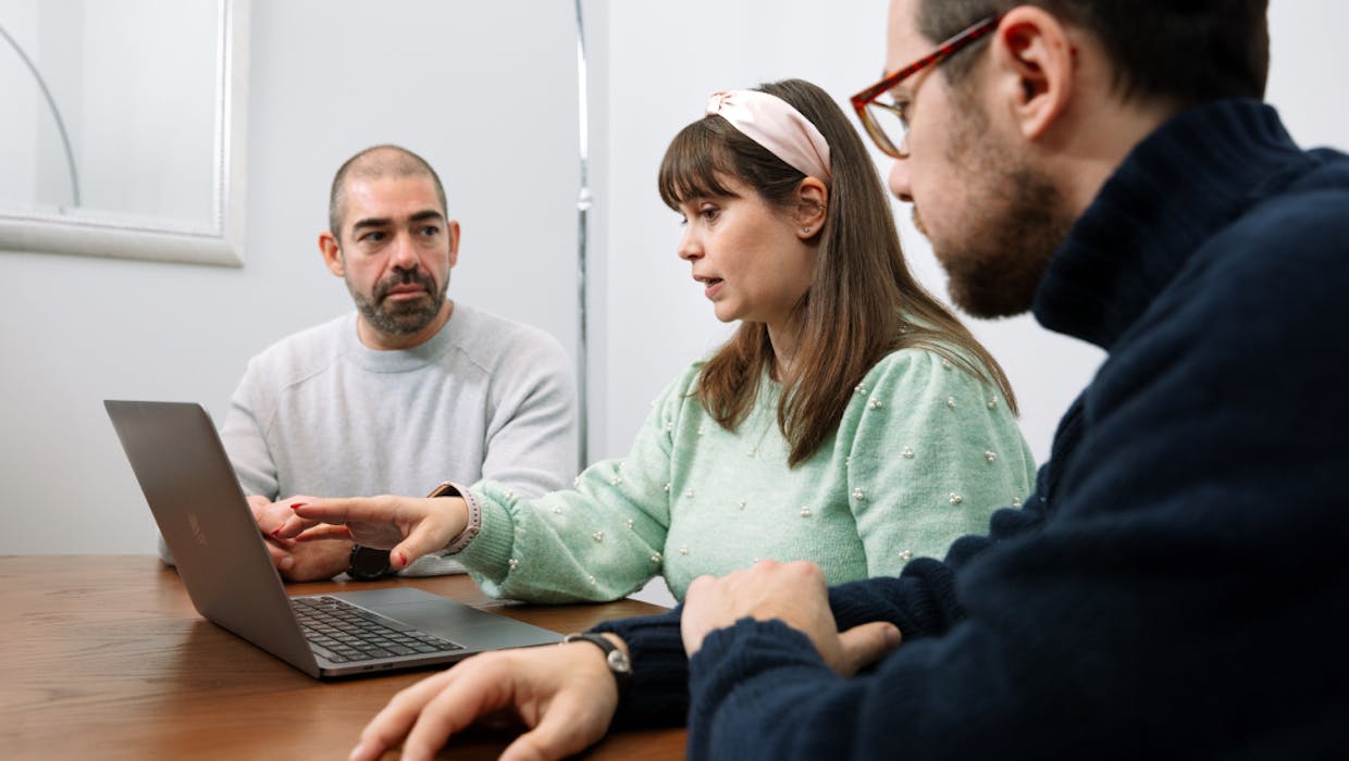 Three people in an office setting talking in front of a computer.