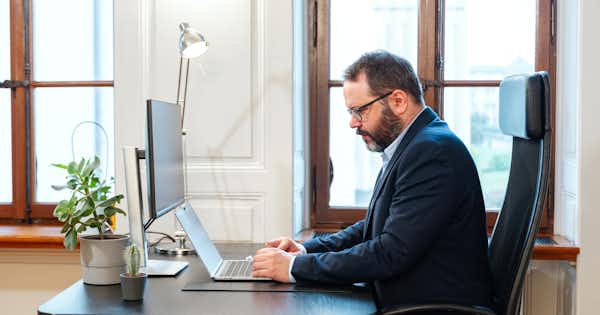 Photo showing a man in side profile, seated and working on a computer.