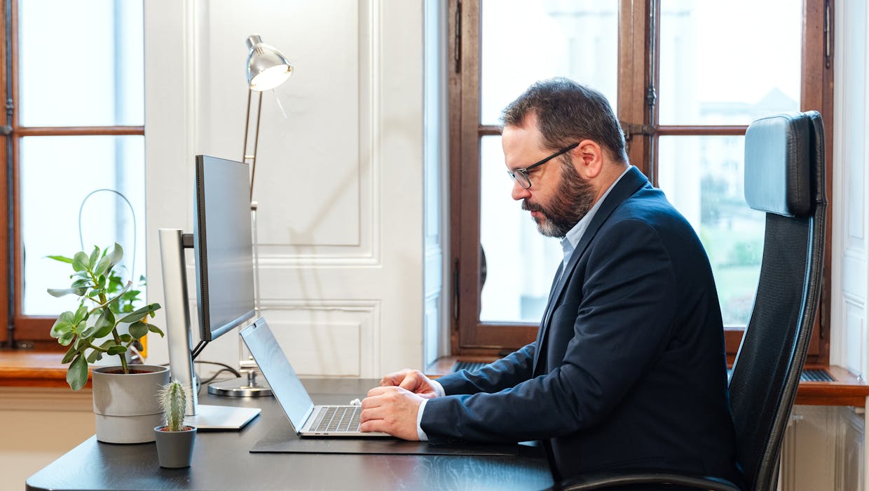 Photo showing a man in side profile, seated and working on a computer.