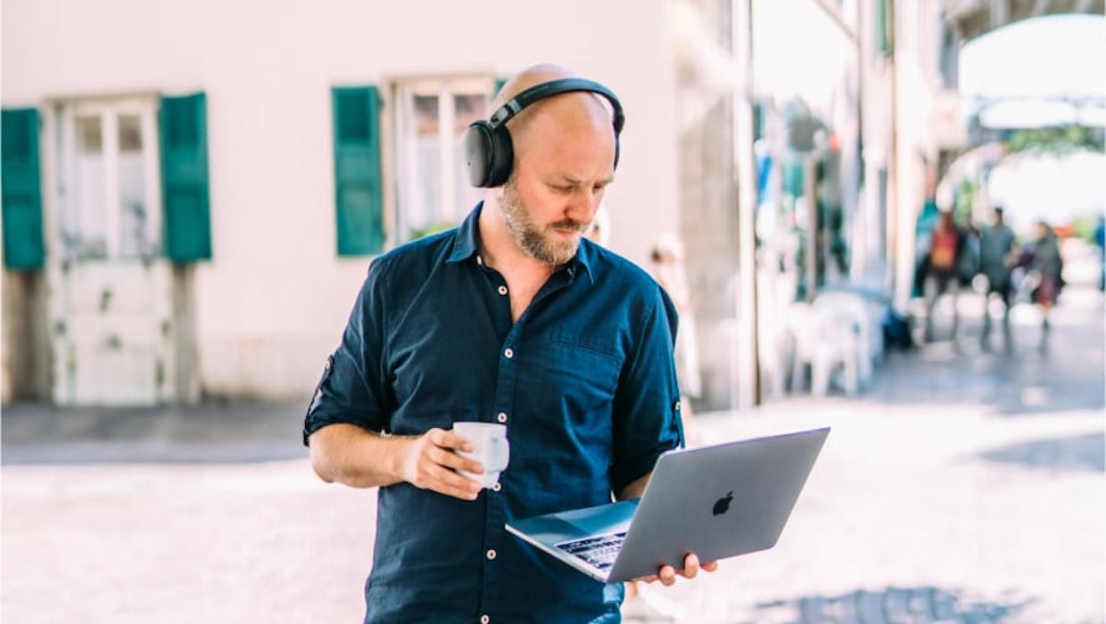 Homme tenant une tasse dans une main et un ordinateur portable dans l'autre.