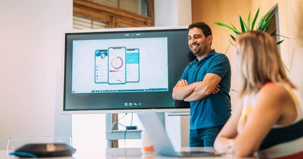 Man in front of room presenting data on a big screen.