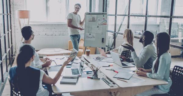 Team of people at a conference table with someone presenting on whiteboard