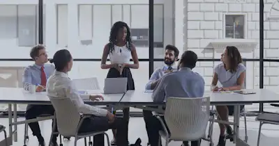 Des employés assis à une table de conférence, l'un d'entre eux est debout et parle.