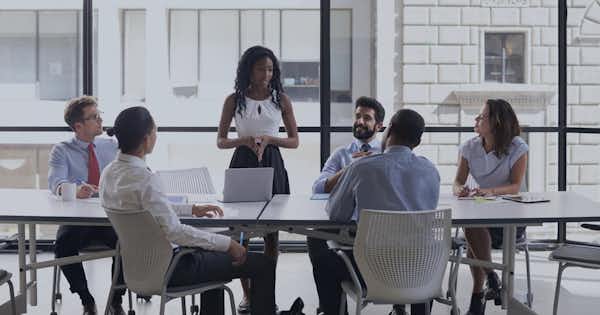 Employees seated at a conference table, one is standing and talking