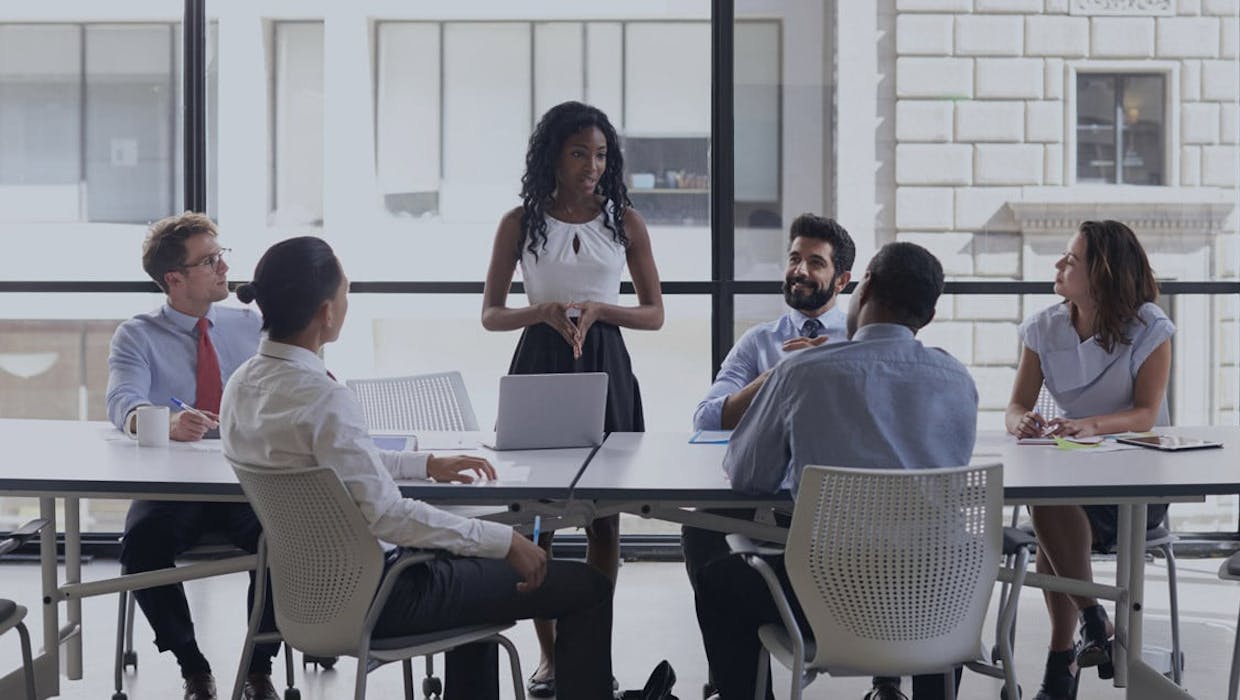 Des employés assis à une table de conférence, l'un d'entre eux est debout et parle.