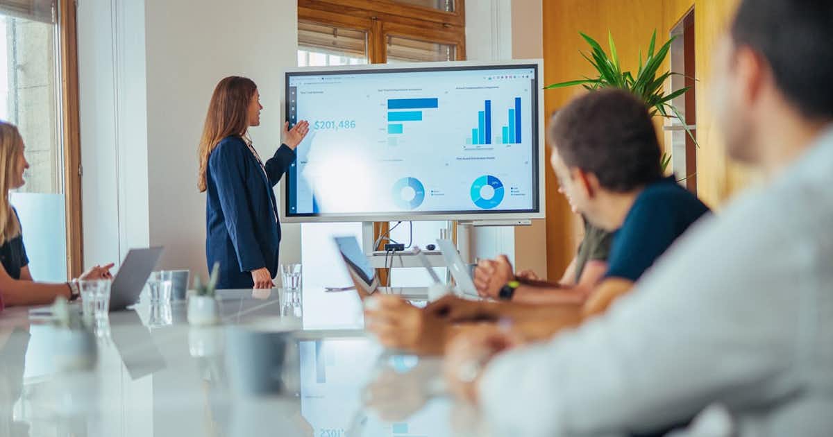 Woman in conference room presenting a dashboard on a big screen