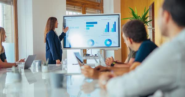 Woman in conference room presenting a dashboard on a big screen