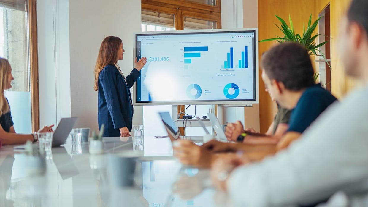 Une femme dans une salle de conférence présentant un tableau de bord sur un grand écran.