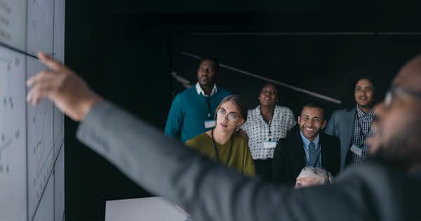 Homme montrant des chiffres sur un tableau devant un groupe