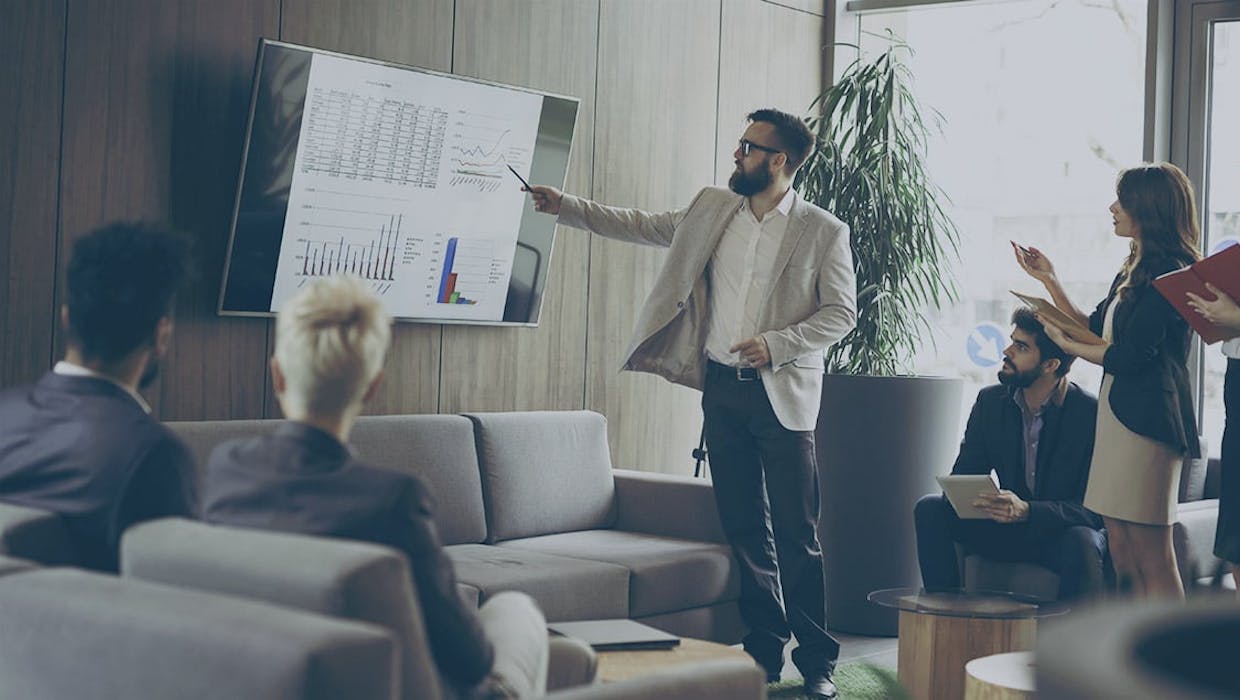 Un homme montrant des chiffres sur un grand écran devant un groupe.