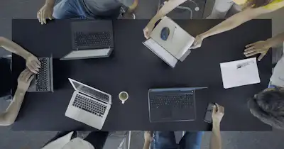 Overhead view of laptops on a table with people sitting around it.