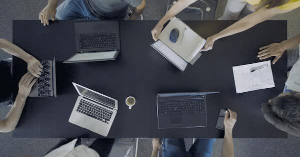 Vue aérienne d'ordinateurs portables posés sur une table autour de laquelle sont assises plusieurs personnes.