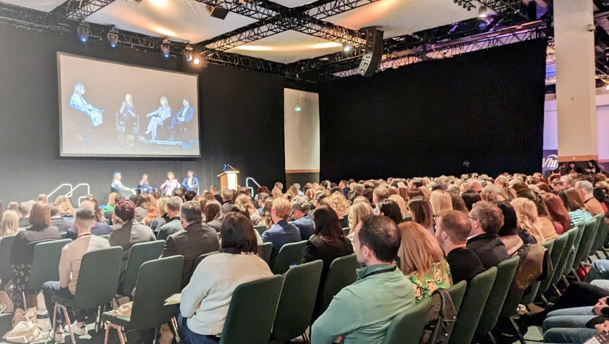 A room full of people facing a stage at a conference.