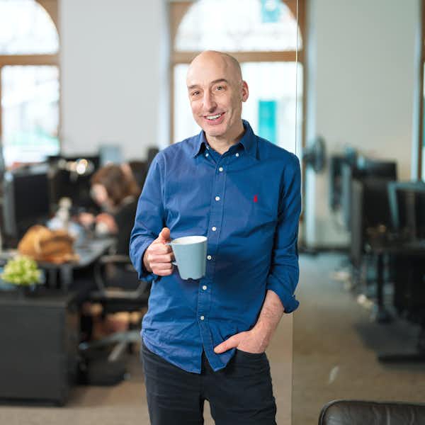 A man in a blue shirt in an office holding a coffee cup.